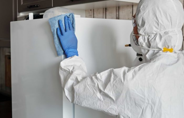 A woman in a protective gear is wiping down and deep cleaning the fridge.