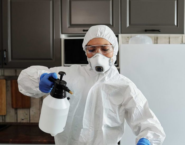 A woman in protective gear is holding a spray bottle and sanitizing the surface in front of her.