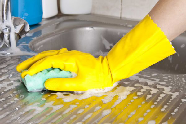 A hand in a yellow glove cleaning the sink.